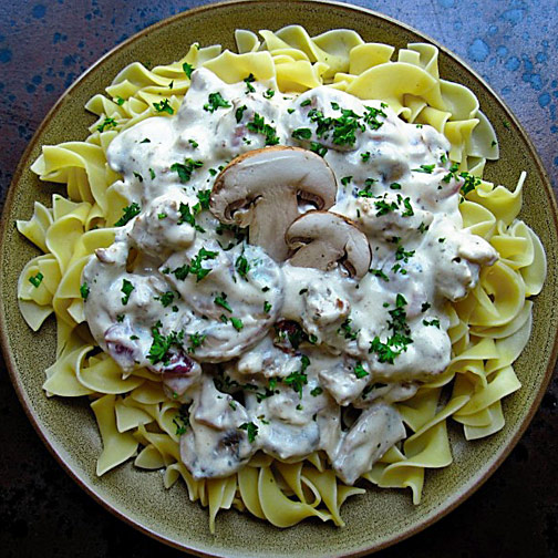 A plate of delicious sausage stroganoff topped with cheese, basil and mushrooms