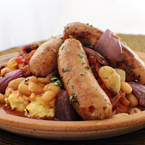 A plate of polenta topped with roasted veggies, white beans, and Premio sweet chicken sausage