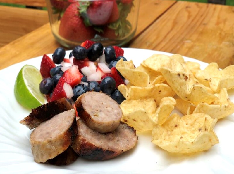 Sliced Premio sausage served with a strawberry, blueberry, and onion salsa and chips