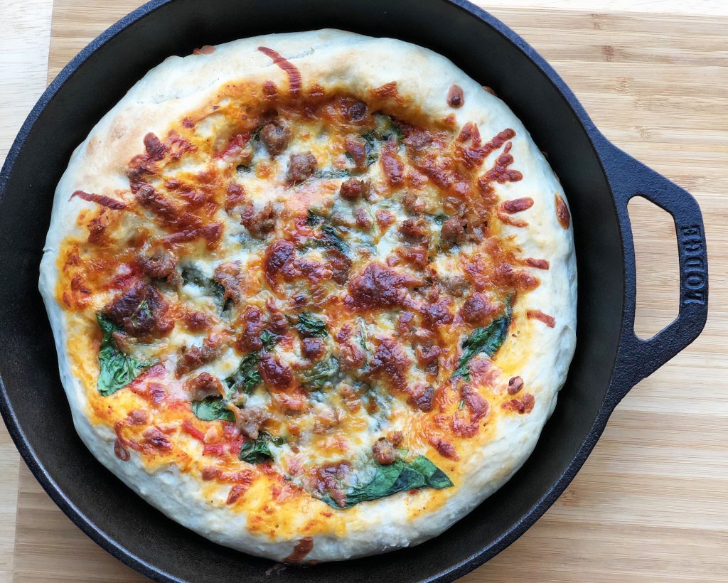 A pizza topped with spinach and Premio sausage in a skillet pan