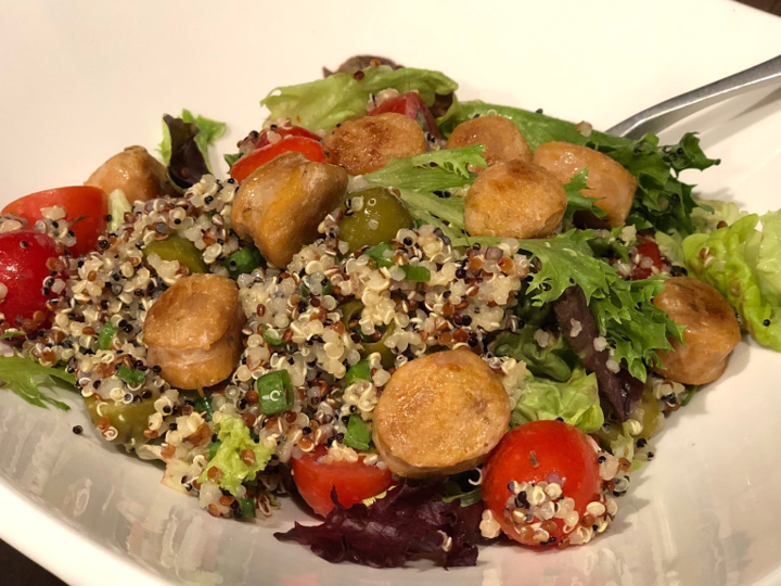 Enjoy a quinoa salad bowl topped with sliced sausage, cherry tomatoes and olives