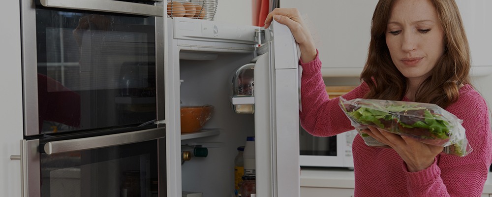 woman putting bag of lettuce in fridge