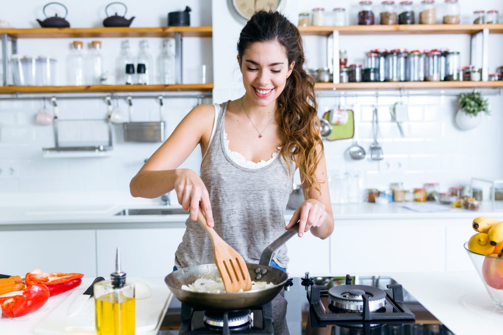 ortrait of young woman frying onion into the pan in the kitchen.