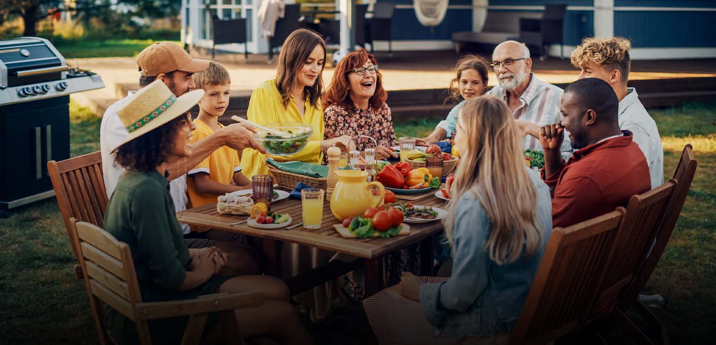 A group of friends and family sitting at a table outside enjoying food from a cookout